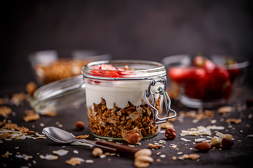 Glass jar of oat granola with yogurt and fresh strawberries for healthy breakfast