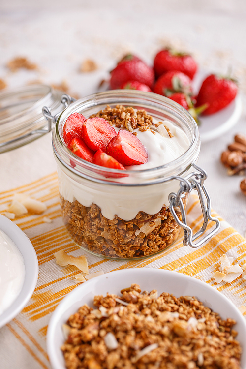 Homemade granola in glass jar layered with yogurt and fresh strawberries