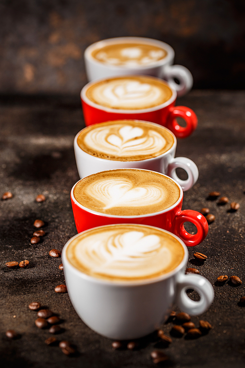 Many cups of cappuccino with latte art on dark background