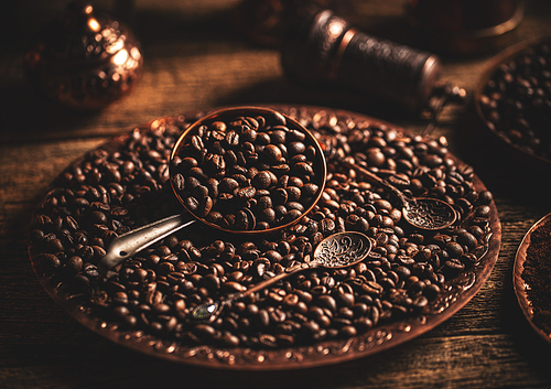 Coffee beans in copper plate with antique spoon on wooden background, dark toned