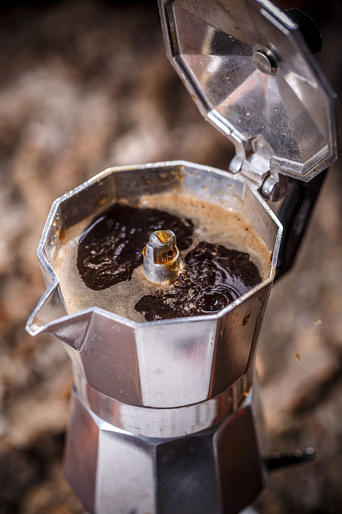 Italian traditional coffee maker with hot coffee flowing out from the spout