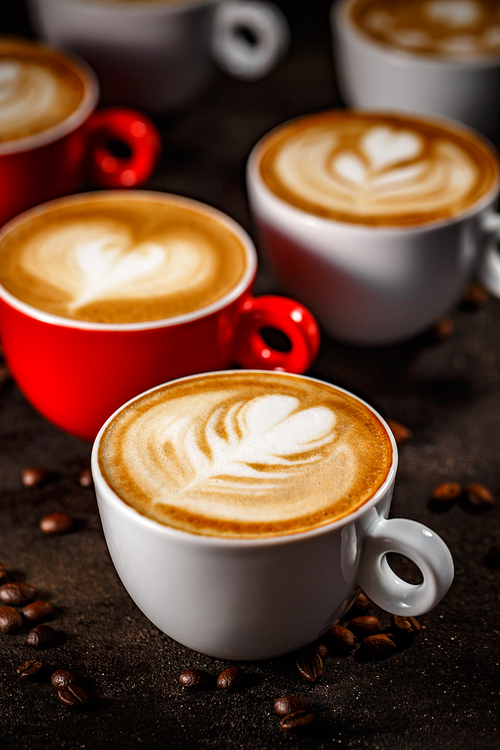 Many cups of cappuccino with latte art on dark background