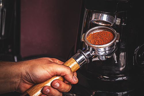 Barista grinding coffee on professional grinder machine in coffeeshop closeup. Preparing for grind and making espresso