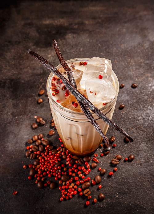 Iced coffee with milk in tall glass spiced with pink peppercorn and vanilla