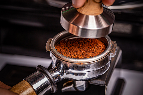 Barista is using a tamper to press freshly ground morning coffee