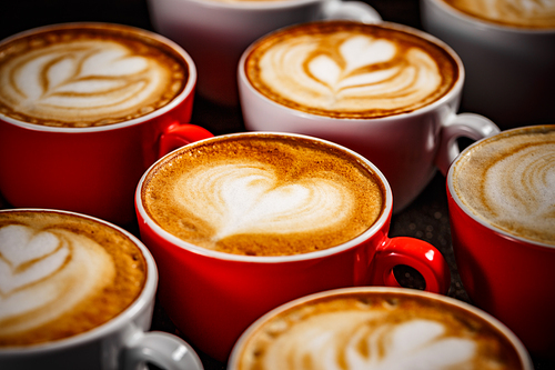 Close up of many cups of cappuccino with latte art on dark background