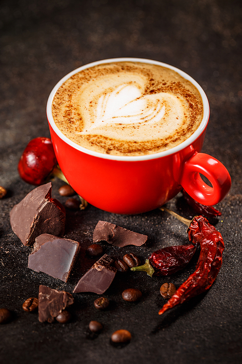 Coffee cup with chili peppers and chocolate on a dark vintage background