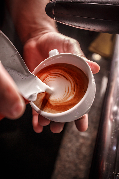 Barista makes coffee latte art, he is pouring milk