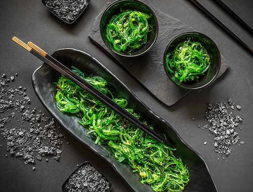 Seaweed wakame salad served with chopstick on black background