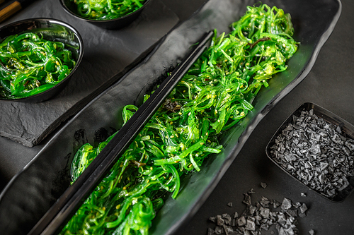 Seaweed wakame salad served with chopstick on black background