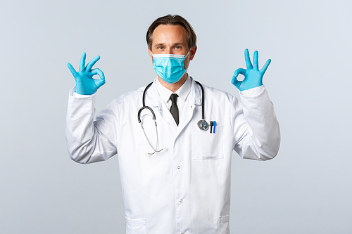 Covid-19, preventing virus, healthcare workers and vaccination concept. Doctor guarantee safety or quality of clinic services, showing okay gesture in approval, wear medical mask and gloves.
