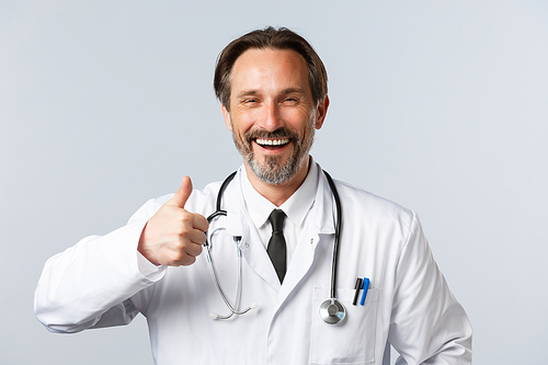 Covid-19, preventing virus, healthcare workers and vaccination concept. Cheerful middle-aged male doctor in white coat laughing happy and thumb-up in approval, recommend product or services.