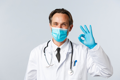 Covid-19, preventing virus, healthcare and vaccination concept. Happy smiling doctor in medical mask and gloves assure all good, show okay sign as guarantee safety and quality of service in clinic.