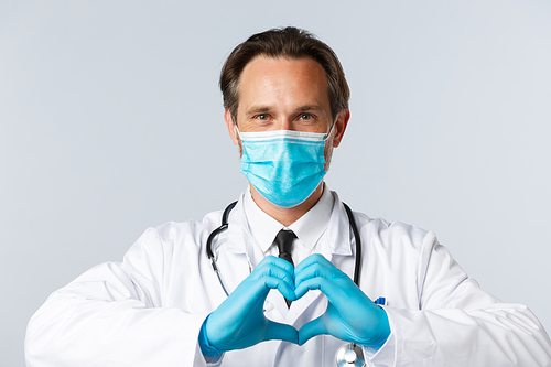 Covid-19, preventing virus, healthcare workers and vaccination concept. Close-up of caring and friendly doctor in medical mask, gloves, taking care patients health, showing heart sign.