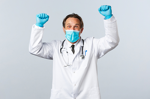 Covid-19, preventing virus, healthcare workers and vaccination concept. Happy excited doctor in medical mask and gloves raise hands up shouting yes, winning, celebrating victory or achievement.
