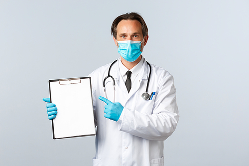 Covid-19, preventing virus, healthcare workers and vaccination concept. Professional doctor at clinic pointing at clipboard paper, explain disease or showing chart, wear medical mask and gloves.