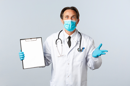 Covid-19, preventing virus, healthcare workers and vaccination concept. Shocked and concerned male doctor in medical mask and gloves, showing test results on clipboard.