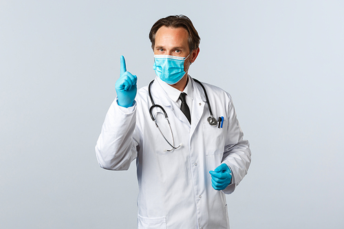Covid-19, preventing virus, healthcare workers and vaccination concept. Professional middle-aged doctor in medical mask and gloves showing finger, explain rules during coronavirus social distancing.