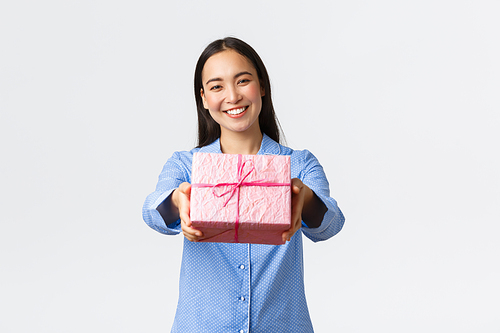 Home, holidays and lifestyle concept. Lovely smiling asian sister in blue pajama giving you gift for birthday or christmas celebration, congratulate with bday sibling, white background.