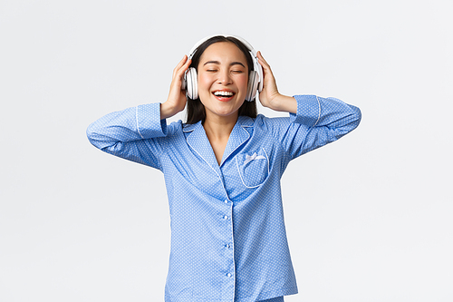 Home leisure, weekends and lifestyle concept. Happy pleased asian woman in pajamas enjoying awesome sound quality in new earphones, dancing in pajamas and listening music.