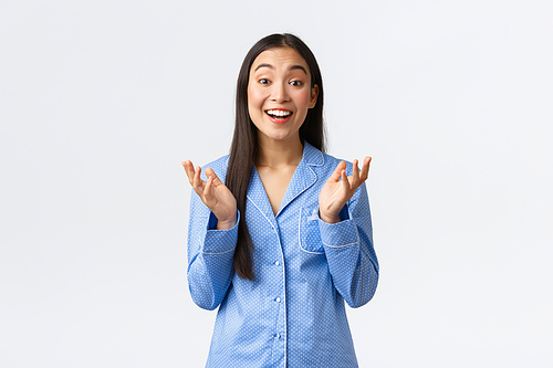Happy beautiful asian girl in blue pajamas raising hands and clapping in amusement, smiling amazed, listening to wonderful news, praising good work, standing in jammies over white background.