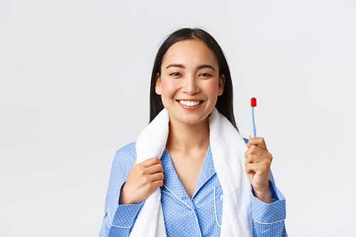 Daily routine, morning and hygiene concept. Smiling happy pretty asian girl going to bathroom with towel, wearing pajama, holding toothbrush and showing perfect white smile.