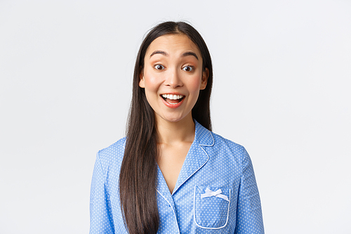 Close-up of enthusiastic and upbeat asian girl in blue pajama looking with thrill at camera. Female student in jammies hear great announcement, being interested in promo, white background.