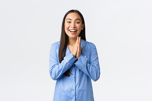 Hopeful and pleased asian girl in blue pajamas smiling delighted, rubbing palms as relish great outcome or profit, feeling lucky, awaiting for good news, standing white background.