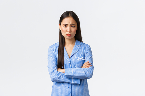 Offended silly insecure asian girl in blue pajamas, cross hands chest and sobbing, pouting and frowning from unfair situation, feeling insulted and sad, standing timid over white background.