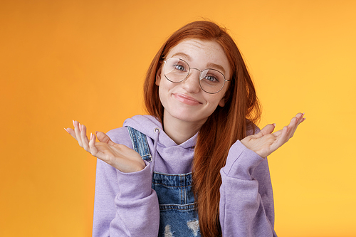 Nothing much. Attractive silly unsure carefree redhead unbothered cute female wearing geek glasses smirking uncertain shrugging hands spread sidways clueless what do future, orange background.