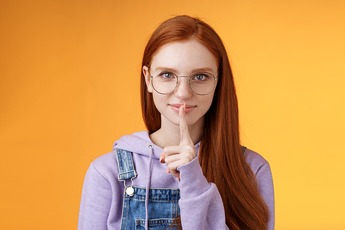 Shh secret safe. Young sensual mysterious redhead attractive woman hiding info say shush silence quiet please prepare surprise hold index fingers mouth taboo, standing orange background.