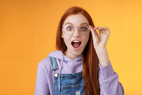 Omg so cool. Portrait amazed speechless excited redhead girl drop jaw amused stare camera surprised find out awesome product net touch glasses reading impressive post, orange background.
