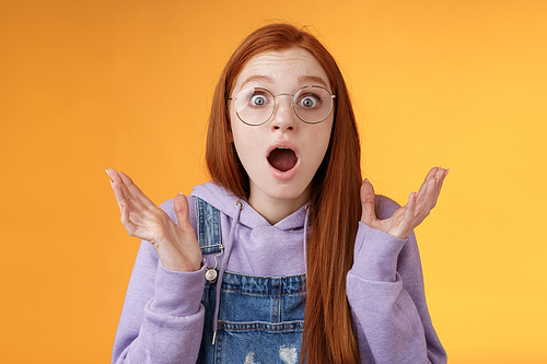 Close-up shocked sensitive concerned young panicking redhead woman worry drop jaw gasping raise hands spread freak out stare surprised emotional reacting incredible news, orange background.