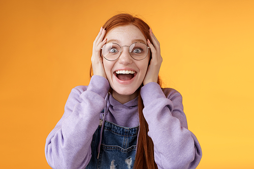 Impressed lucky cute redhead girl winner cannot believe dream come true win awesome present standing happily excited grab head smiling broadly open mouth stare surprised amazed, orange background.