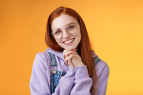 Tender romantic lovely redhead girlfriend leaning palms tilting head cute flirty giggling smiling camera white teeth wearing glasses hoodie overalls near orange background, sensually laughing.