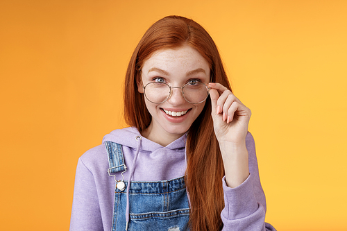 Charming silly modest young redhead female geek game lover discus last gaming trends smiling happily amused touch glasses grinning curiously receive cute gift surprised, orange background.