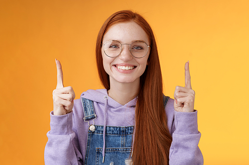 Lively charismatic pleasant redhead female student helpful pointing up index fingers showing awesome promo offer smiling delighted white teeth indicating advertisement recommend use product.