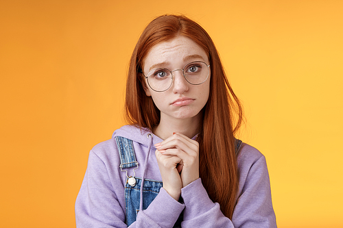 Pretty please. Clingy young sad sulking redhead girl sibling wearing glasses pouting silly press palms begging gesture pleading wanna receive help promise be good ask favour, orange background.