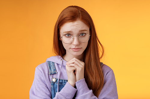 Silly guilty young shy redhead girlfriend asking forgiveness supplicating lower head look from under forehead frowning begging apology favour standing insecure sad pleading help, orange background.