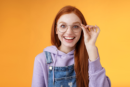 Happy enthusiastic young redhead girl amused find out excellent place celebrate b-day standing joyful excited touch glasses smiling broadly white teeth grinning rejoicing surprised, orange background.
