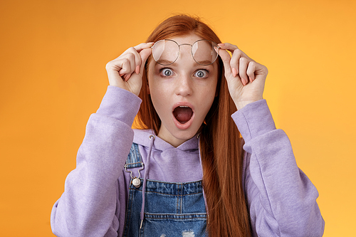 Omg no freakin way. Shocked emotional redhead girlfriend take off glasses speechless drop jaw gasping stunned wide eyes camera stare amazed found out shook secret standing orange background.