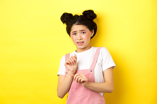 Stay away. Reluctant timid asian girl step back, raising hands to block something disgusting, grimacing displeased, say no, rejecting with aversion, yellow background.