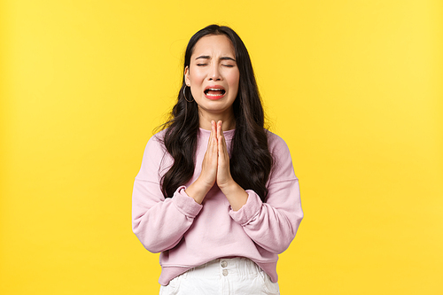 People emotions, lifestyle and fashion concept. Desperate and sad gloomy asian girl begging for forgiveness, crying heart out and praying, pleading god mercy, standing yellow background.