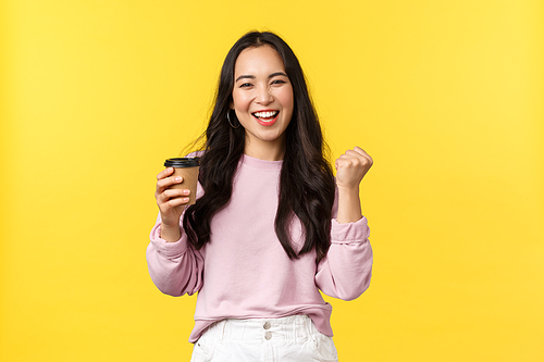 People emotions, lifestyle leisure and beauty concept. Enthusiastic and energized smiling asian woman drinking cup of tasty coffee from best cafe takeaway, fist pump happy, got pumped up.