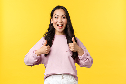 People emotions, lifestyle and fashion concept. Ambitious and excited smiling asian woman show thumbs-up in approval, agree or supports great idea, congratulate or praise friend, yellow background.