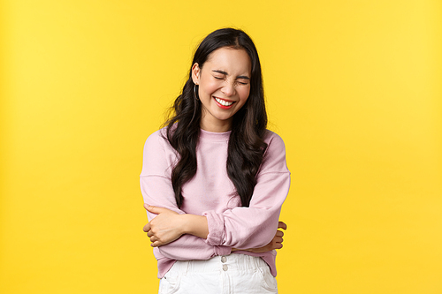 People emotions, lifestyle and fashion concept. Happy carefree smiling asian woman chuckle, touch belly and laughing out loud, standing yellow background, hear good joke.