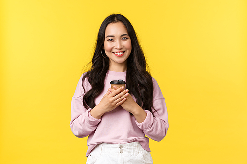 People emotions, lifestyle leisure and beauty concept. Lovely asian woman with cup of takeaway coffee enjoying summer weekends, smiling delighted and cute, drinking beverage over yellow background.