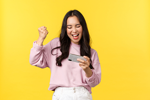 People emotions, lifestyle leisure and beauty concept. Enthusiastic asian girl gamer playing on mobile phone, tilting smartphone to pass level in game, smiling amused, fist pump as winning.