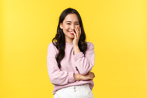 Lifestyle, emotions and advertisement concept. Beautiful and happy romantic asian girl giggle, hold hands over mouth while smiling, looking at something adorable and silly, yellow background.