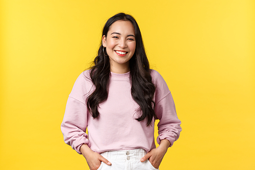 People emotions, lifestyle and fashion concept. Cheerful good-looking korean girl having fun, laughing and feeling happy, standing joyful over yellow background.